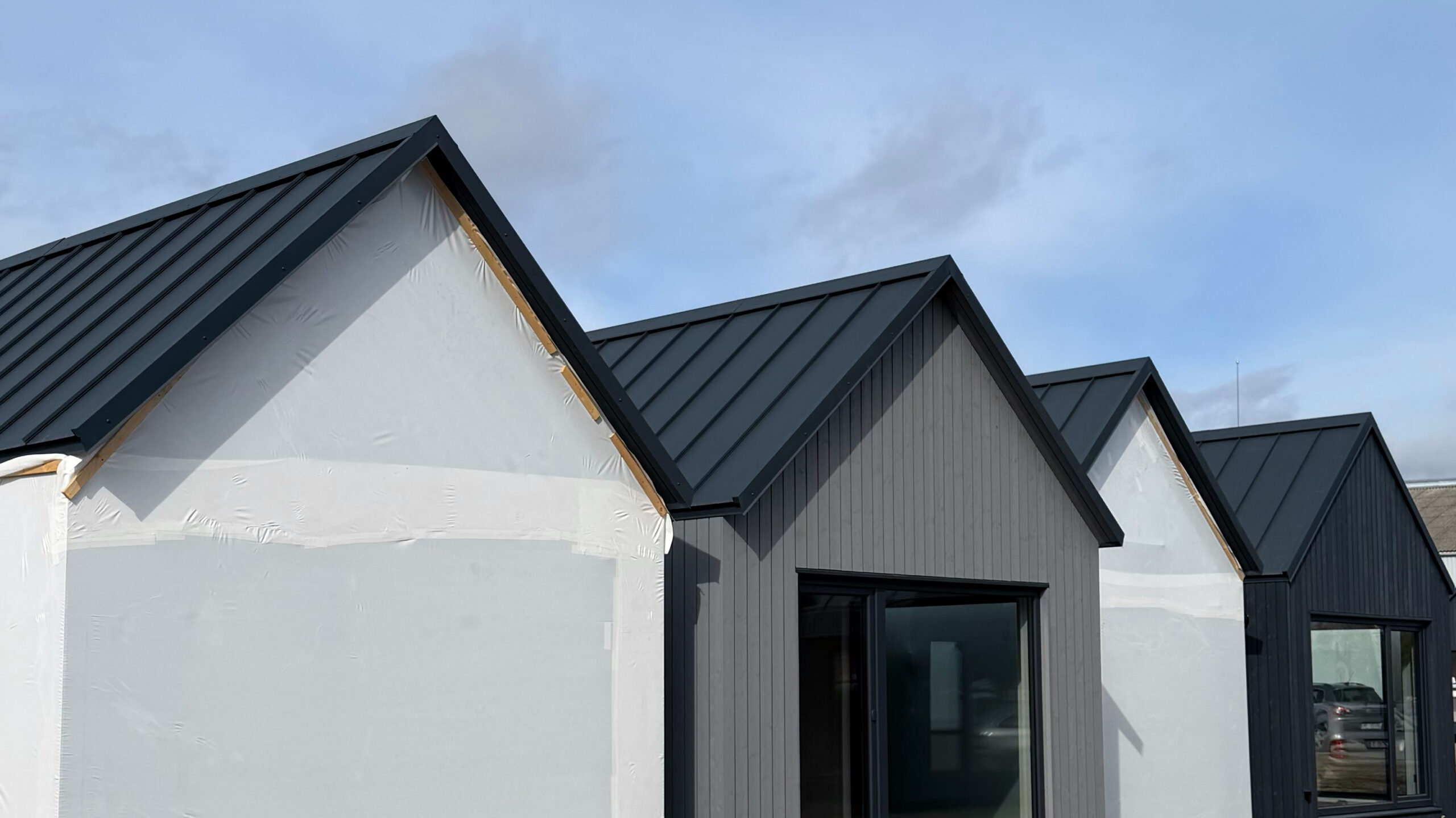 A row of finished MyCabin homes with black standing-seam roofs and timber cladding