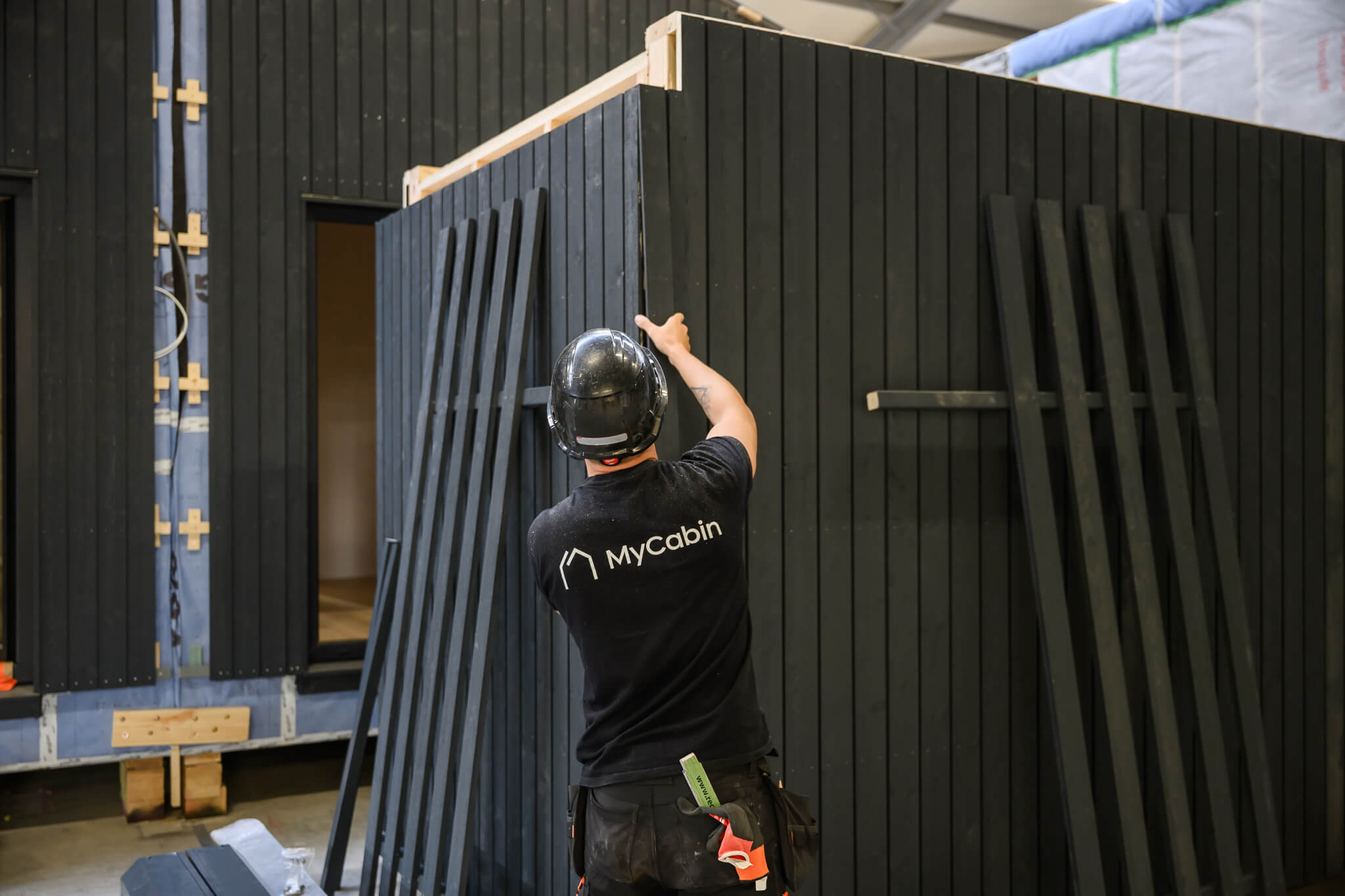 A MyCabin team member fitting black timber cladding to a home at the factory